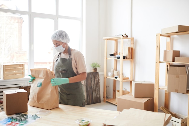 female worker wearing protective clothing while packaging orders at food delivery service