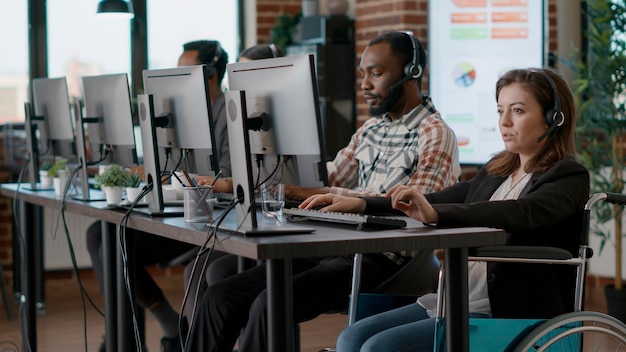 Photo female worker in wheelchair working on telecommunications, answering helpline calls at customer support service. woman talking to people on audio headset with microphone at clients care.