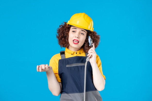 Female worker in yellow uniform using shower as a phone on blue