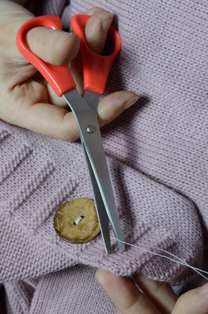 Foto le mani delle lavoratrici cuciono un bottone di legno su una giacca. avvicinamento.