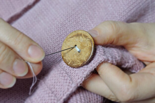 Female workers' hands sew a wooden button to a jacket. close-up.