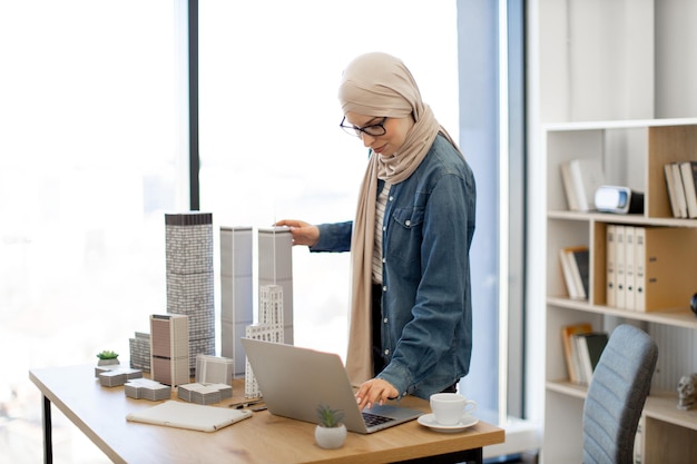 Женщина работает на ноутбуке, стоя рядом с масштабными моделями
