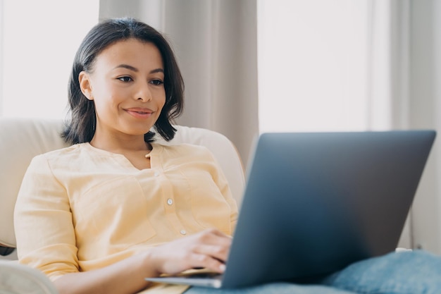 Female works at laptop sitting in chair at home office shopping online Ecommerce ebusiness