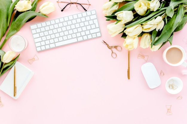 분홍색 배경에 컴퓨터 튤립 꽃 부케 황금 액세서리 일기가 있는 여성 작업 공간