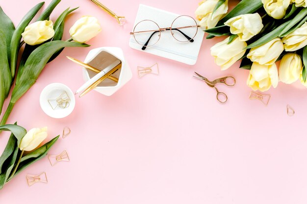 Female workspace with tulip flowers bouquet golden accessories diary on pink background flat lay