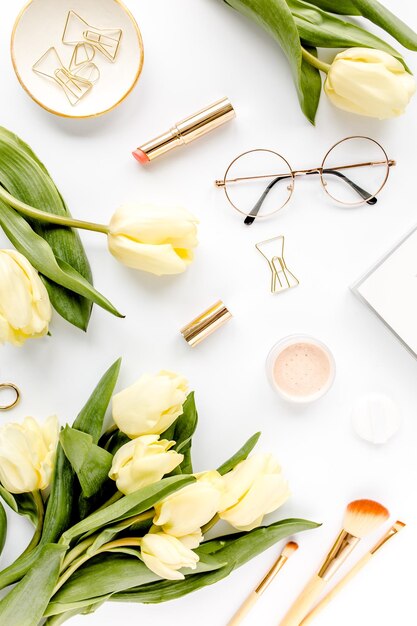 Female workspace with yellow tulip flowers womens fashion golden accessories diary glasses on white