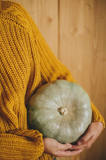 Foto donna in maglione lavorato a maglia giallo che tiene zucca verde su fondo di legno rustico ciao autunno e felice ringraziamento che celebra le vacanze autunnali a casa accogliente raccolto autunnale