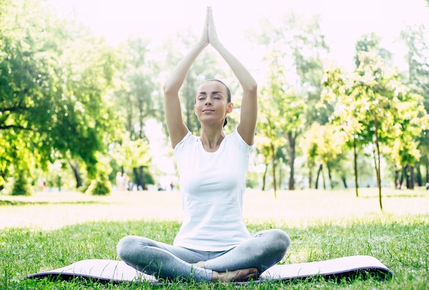 Female Yoga at park. Young brunette woman in lotus pose sitting on green grass in park. Concept of calm and meditation