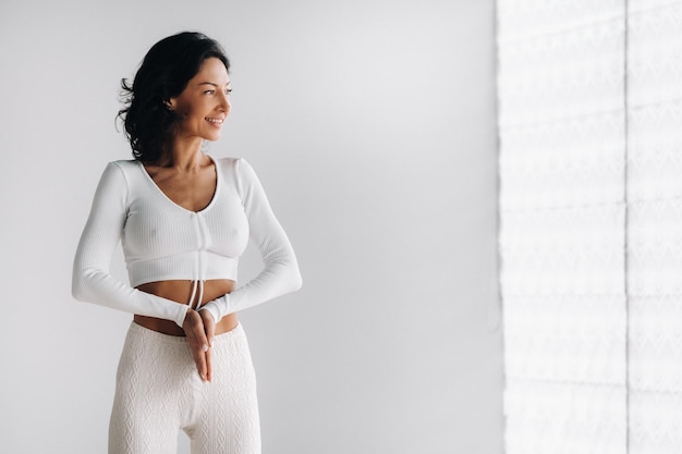 A female yogi in white clothes stands with her hands clasped at the bottom meditating in the yoga hall