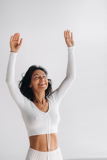 A female yogi in white clothes with her hands up meditates in the Yoga hall
