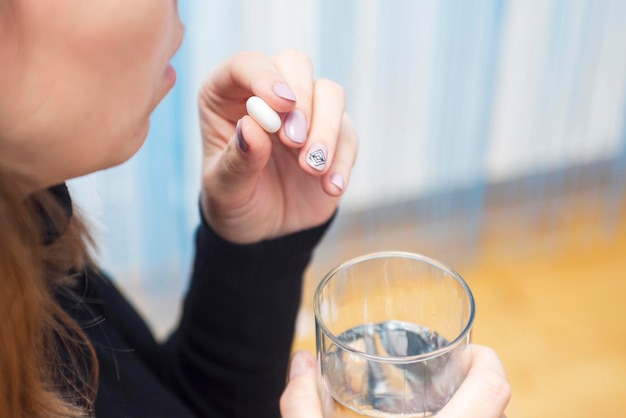 Females hands are holding one tablet and glass of water close up