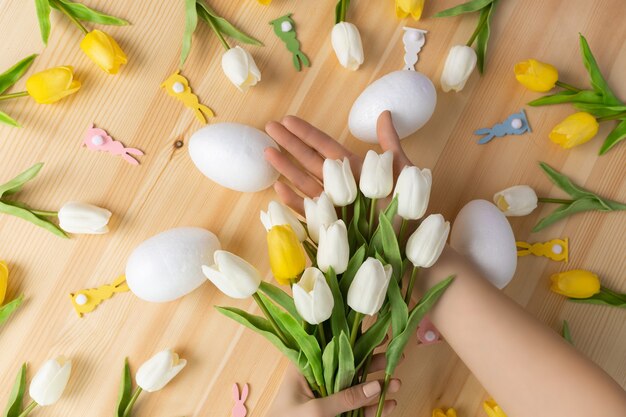 Females hands holding bouquet of fresh tulip flowers on wooden pink background, flat lay composition with copy space