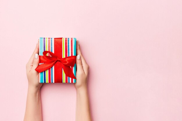 Photo females hands holding striped gift box with colored ribbon on coral background christmas concept