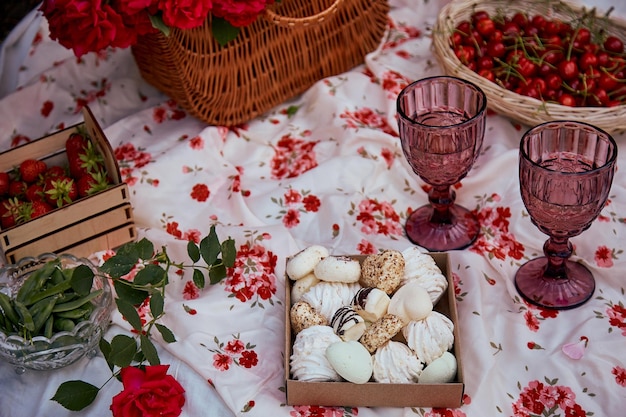 Feminine aesthetic summer picnic with pink tablecloth\
marshmallow strawberries glasses of wine among pink roses in the\
park romantic evening travel and appreciation of the moment\
selective focus