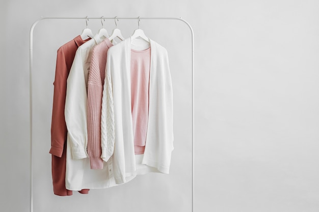 Feminine clothes in pastel pink  color on hanger on white background.  Elegant dress,  jumper, shirt and other fashion outfit. Spring cleaning home wardrobe. Minimal concept.