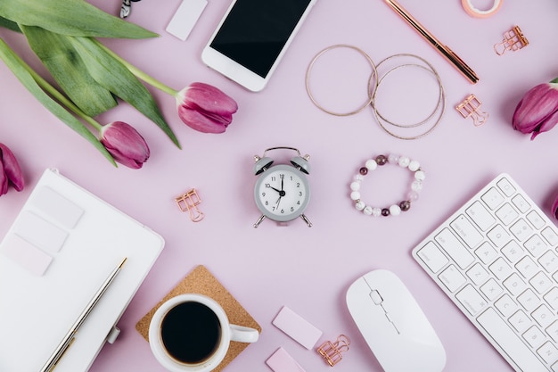 Feminine desk workspace with tulips, keyboard, glasses, golden clips on violet