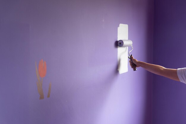 Feminine hand paints wall that had been formerly decorated with tulip shaped stencils