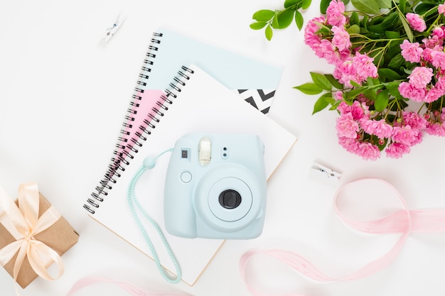 Feminine home office desk with modern instant film camera,paper notebook and notepad, bouquet of pik flowers, gift box, ribbon