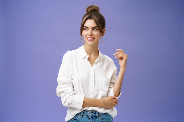 Feminine and stylish modern charming girl with gapped teeth and\
pimple posing in trendy white blouse and round earrings gazing left\
charmed and sensual with cute smile over purple wall.