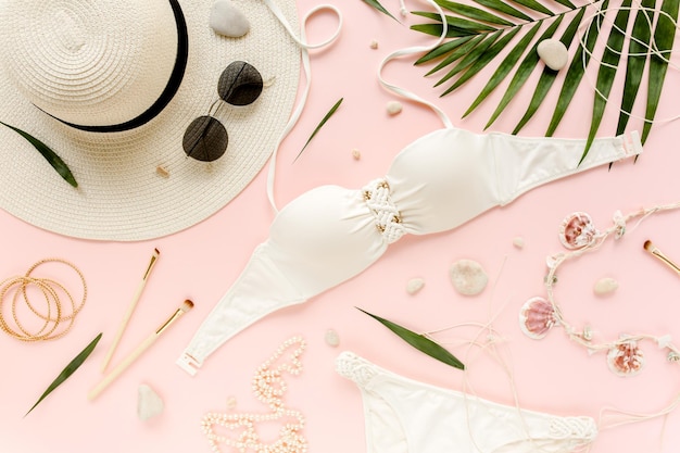 Feminine white swimsuit beach accessories tropical palm leaf branches on pink background travel vaca