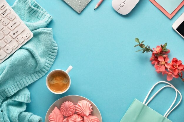 Feminine working space with cotton sweater, keyboard, mobile phone, plate of marshmallow and cup of coffee