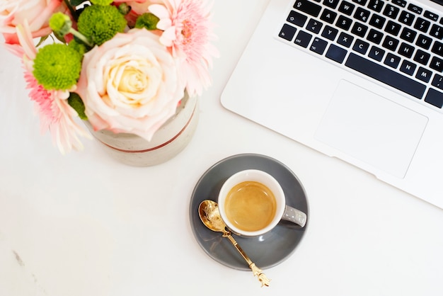 Feminine workplace concept in flat lay style with laptop, coffee, flowers. top view, bright, pink and gold