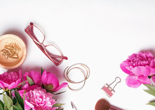 Feminine workplace concept with pink peonies, stationery and glasses