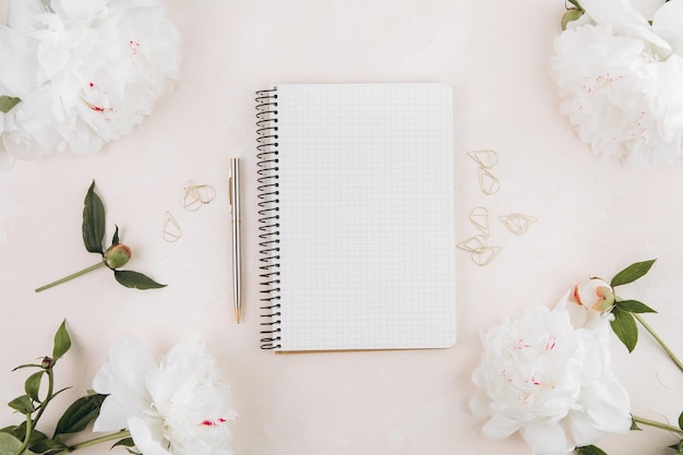 Feminine workspace with blank open notepad and peony flowers stylish office writing supplies and on a pastel teble