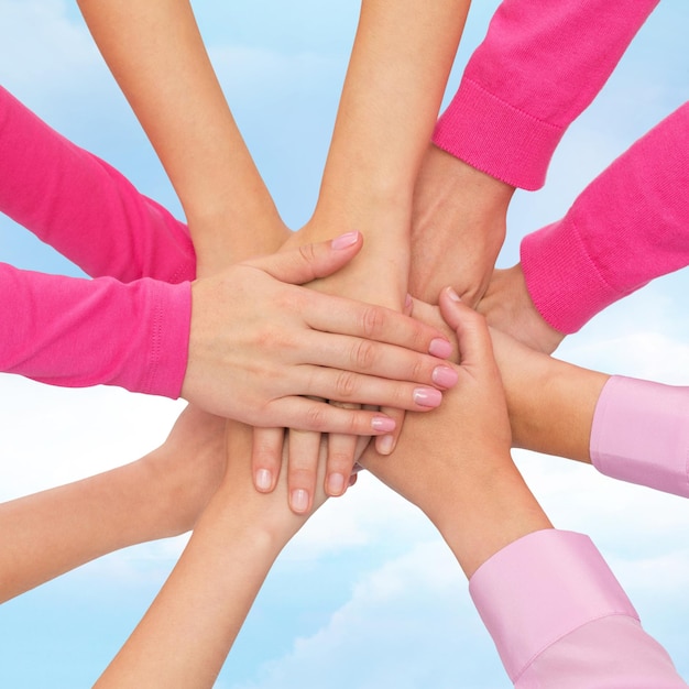 feminism, women power and breast cancer awareness concept - close up of women hands on top of each other over white background