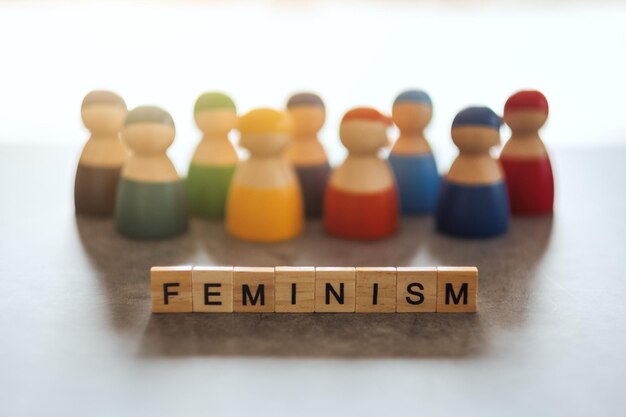 Feminisme woord op houten blokken met een groep vrouwen op de achtergrond