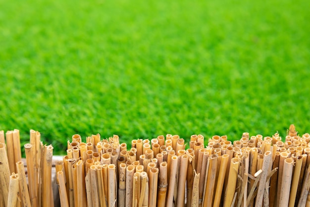 Fence made of dry bamboo stalks against background of artificial lawn grass