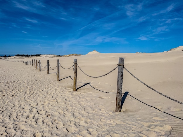 A fence in the sand with a blue sky in the background