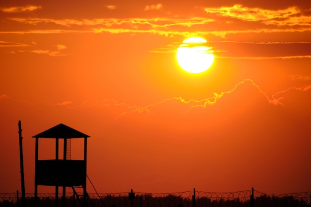 有刺鉄線と古いものみの塔背景明るい太陽と緋色の夕日とフェンス