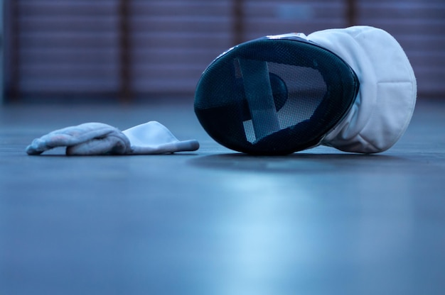 A fencing mask and a fencing glove on the floor