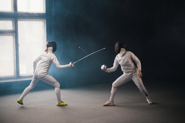 A fencing training two women in protective costumes having a duel