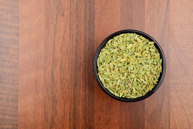 Fennel seeds in bowl on wooden background, dry spice.