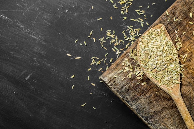 Fennel seeds on a wooden spoon on a black background. 