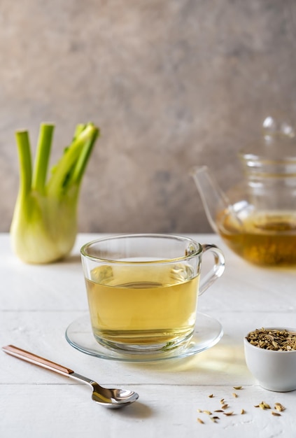 Fennel tea in a glass cup fresh fennel bulb seeds and tea pot on white wooden table