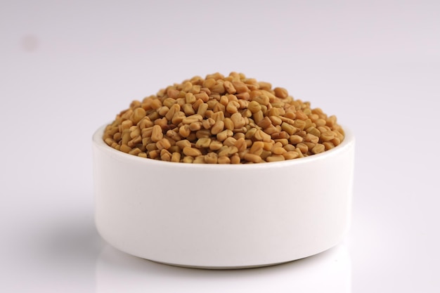 Fenugreek seed Indian spicearranged in a white bowl with white textured background