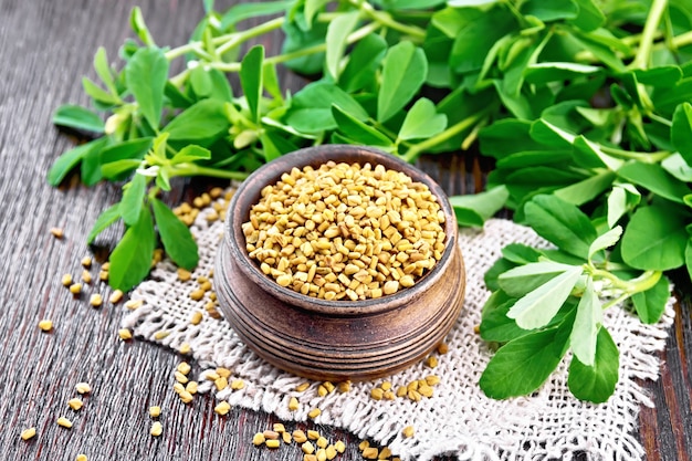 Fenugreek seeds in a bowl on burlap with green leaves on wooden 