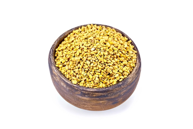 Fenugreek seeds in a brown clay bowl isolated on white