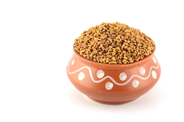 Fenugreek seeds in clay pot isolated on white background