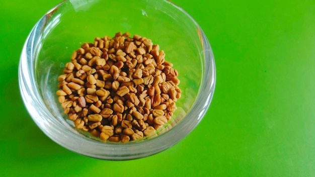Fenugreek seeds in a glass bowl with a green background.