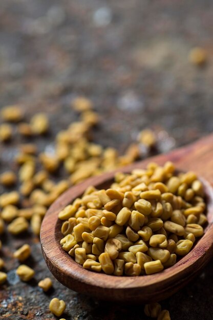 Photo fenugreek seeds in wooden spoon on textured background