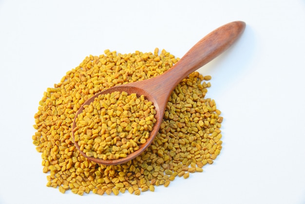 Fenugreek seeds in wooden spoon on White background