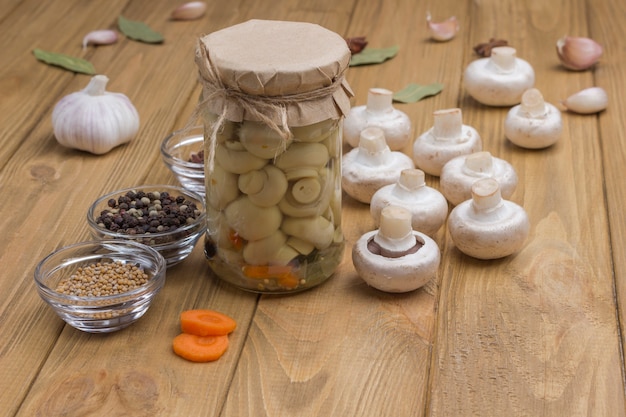 Fermentatieproducten. glazen pot met champignons in blik en verse champignonpaddestoelen. kruid: knoflook, ui, laurier op tafel. gezond wintervoedsel, licht houten oppervlak. kopieer ruimte