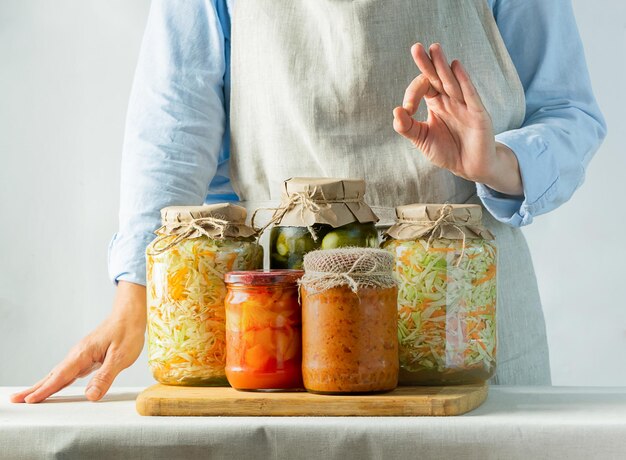 写真 発酵野菜と缶詰の野菜 さまざまな缶がテーブルの上に立ち、女性がエプロンで料理をしています リサイクル 秋の収穫