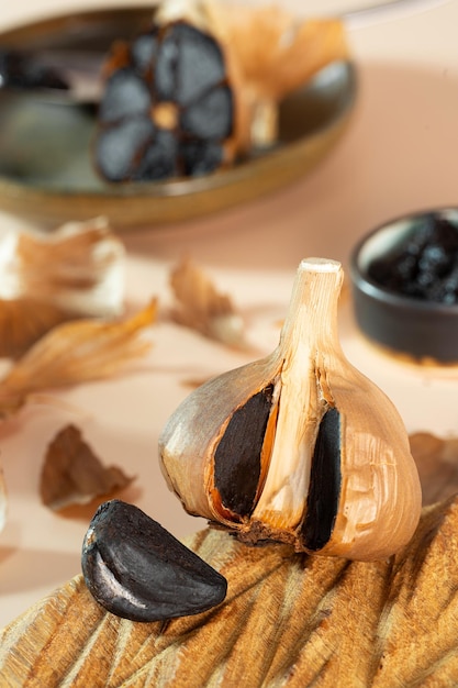 Fermented garlic head and garlic clove on a handmade wooden\
plate a small clay bowl with black garlic paste in the background\
healthy and fermented food photo composition selective focus