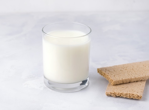 Fermented milk product drink kefir in a glass on a white plate next to snacks.