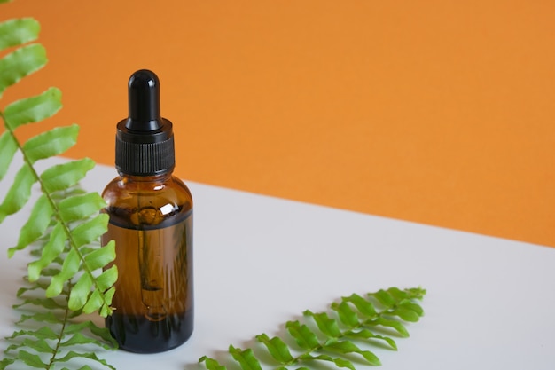 Fern leaves and brown glass dropper bottle on gray and brown background, natural cosmetics concept, body and face skin care, serum or cosmetic oil in a bottle with a dropper